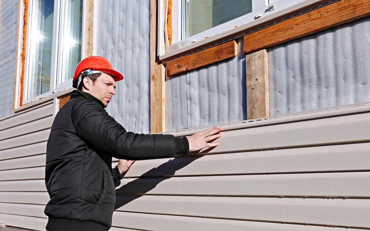 A worker installs vinyl panels beige siding on the outside of house