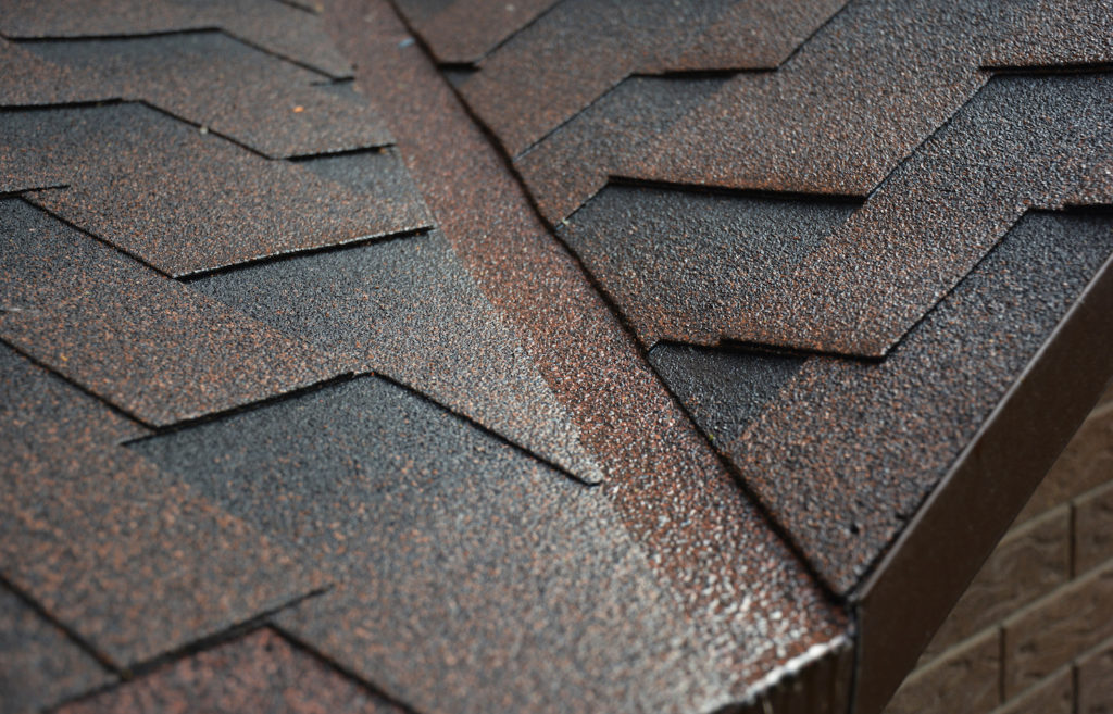 Asphalt shingled roofing construction. A roof valley covered with asphalt shingles with a close-up of a waterproofing flashing in a problem area.