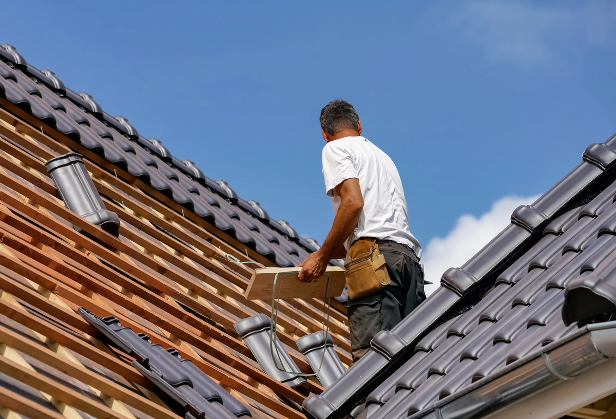 man installing new black tiles on roof