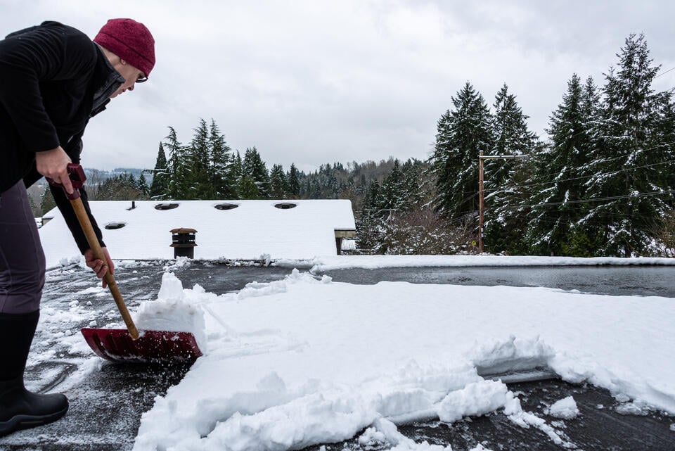how to prevent ice buildup on a flat roof-man shoveling snow off of a residential flat roof
