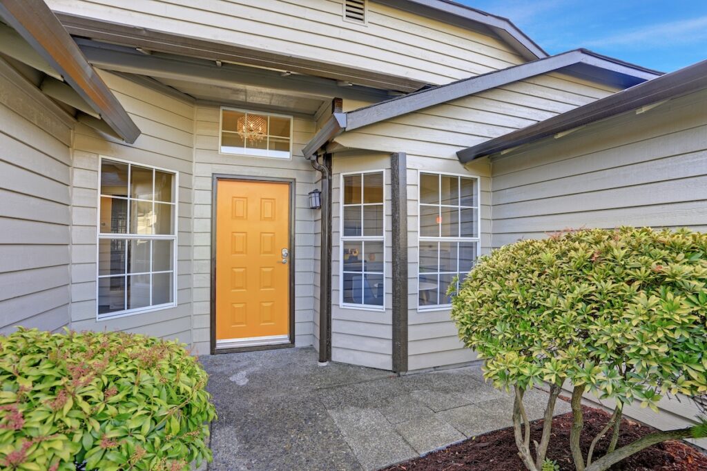 Entrance porch with taupe exterior paint, yellow front door and large windows.